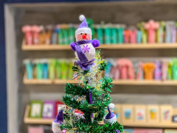 Lila baba hóember a tetején karácsonyfa a könyvesbolt háttér — Stock Fotó