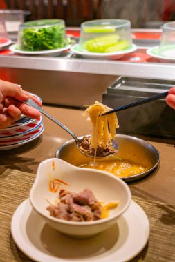 Human using chopsticks and eating enoki mushroom hotpot 