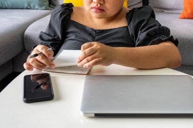 Evde dizüstü bilgisayarı ve çizim defteriyle çalışan tombul bir kadın.