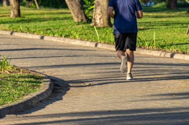 Genç adam güneşli bir günde parkta koşuyor.