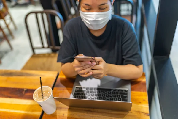 Woman wearing disposable mask while using smartphone in coffee shop