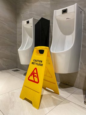 Sarı ıslak zemin uyarı işareti umumi erkek tuvaletinde.