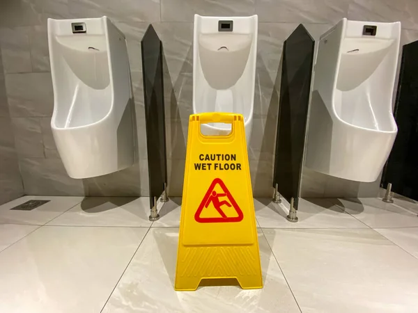 Żółta podłoga mokra znak ostrożności na pisuarach w publicznej toalecie — Zdjęcie stockowe