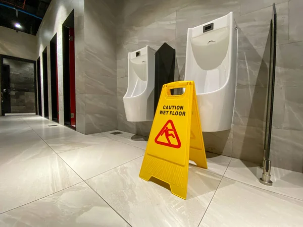 Znak ostrzegawczy na mokrej podłodze w publicznej męskiej toalecie w pobliżu pisuarów — Zdjęcie stockowe