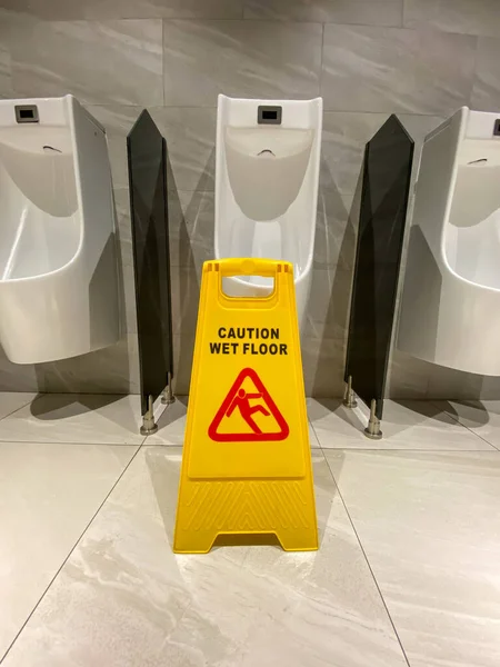 Pionowe zdjęcie znaku ostrzegawczego mokrej podłogi w publicznej toalecie męskiej — Zdjęcie stockowe
