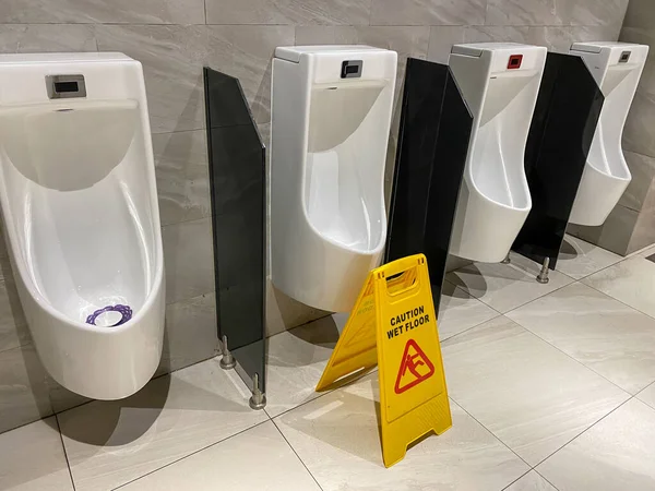 Pisuary i znak ostrzegawczy podłóg mokrych podczas czyszczenia męskiej toalety — Zdjęcie stockowe