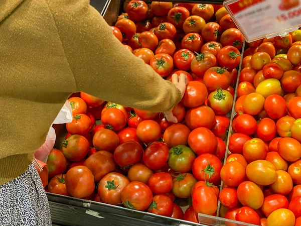 Женщина покупает и выбирает красный помидор в продуктовом магазине — стоковое фото