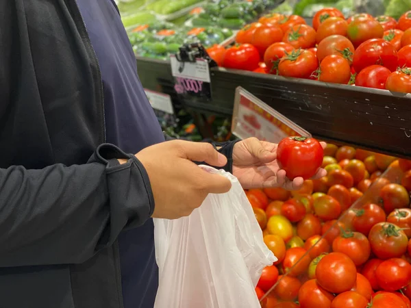 Закрыть фото людей, использующих биопластиковый пакет и покупающих помидоры — стоковое фото