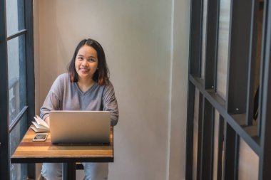 Gülümseyen Asyalı öğrenci kafede ders çalışıyor.