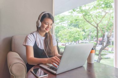 Laptop kullanan, müzik dinleyen genç bir kadın.