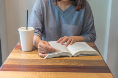 Gri elbiseli genç kadın kitap okuyor, çay içiyor.