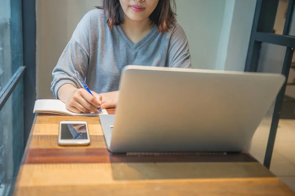 Mujer asiática escribiendo notas y usando laptop — Foto de Stock