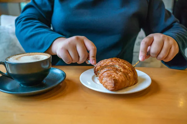 Mädchen isst Croissant und trinkt Kaffee — Stockfoto