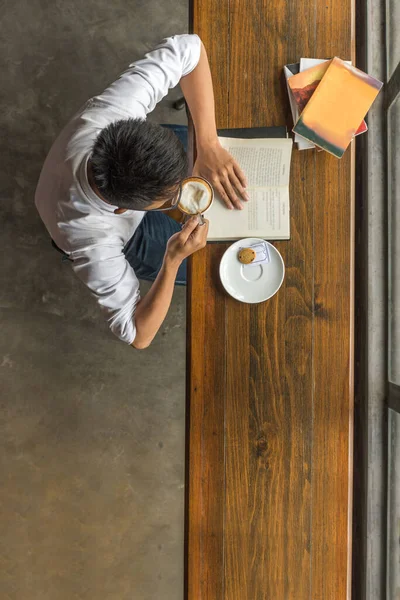 Młody człowiek pijący kawę, czytający książkę za darmo — Zdjęcie stockowe