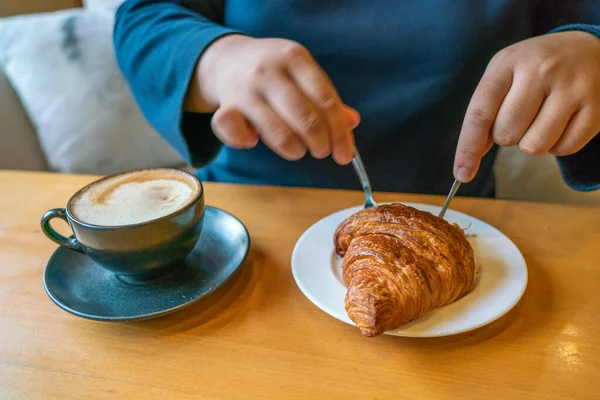 Młoda kobieta je śniadanie z kawą i rogalikiem — Zdjęcie stockowe
