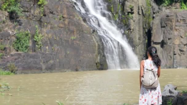 Vrouwelijke toerist in jurk wandelen in de buurt van de prachtige waterval in het regenwoud. — Stockvideo