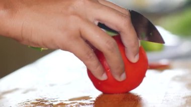 Makro, olgun bir domatesi odun kesme tahtasıyla doğrayan kadınların eline ateş ediyor..