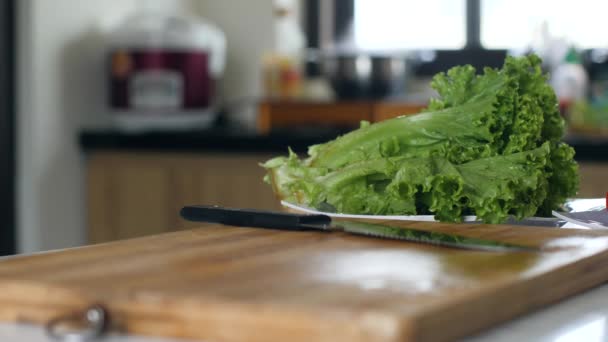 Primer plano de lechuga verde fresca y cuchillo en la tabla de cortar en la mesa de la cocina — Vídeo de stock