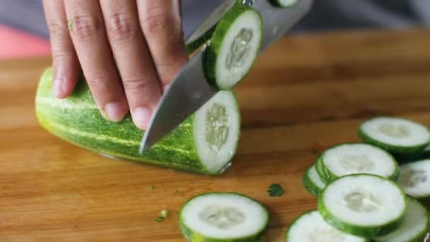 Macro of slicing a fresh cucumber with kitchen knife on a wooden cutting board. — Stock Video