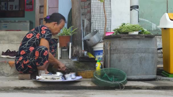 Cham Island, Vietnam, 06 18 2020: En stackars gammal kvinna som rensar och skär fisk på marken utanför sitt hus. — Stockvideo