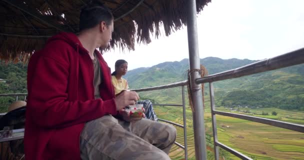 Couple Interracial assis sous un chalet autochtone en plein air profitant de boissons froides. — Video