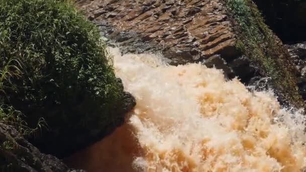 Un fuerte chorro de agua que fluye de entre enormes rocas en la montaña. — Vídeos de Stock