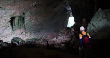 Dışarıdan gelen doğal ışıkla kayalık karanlık bir mağarada yürüyen turistler..