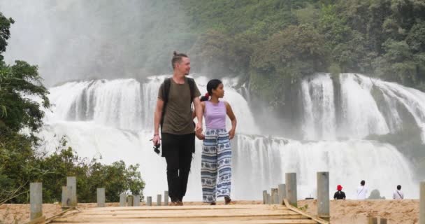 Медленный кадр молодой счастливой межрасовой пары в огромных водопадах backgorund — стоковое видео