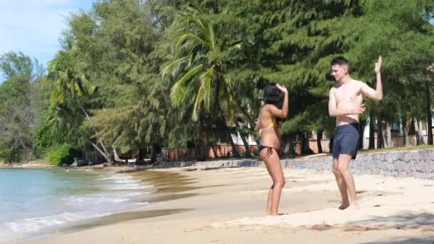 Vidám fiatal terhes pár szórakoztatóan táncol a tengerparton egy napsütéses napon.. — Stock videók