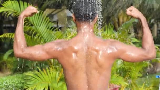 Обратный портрет черного человека, принимающего душ на открытом воздухе на фоне тропических растений. — стоковое видео