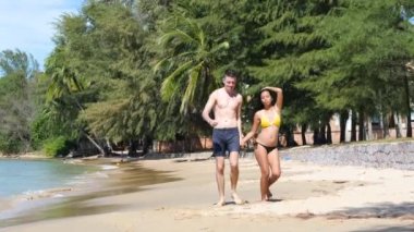 Mutlu ve neşeli genç ırklar arası hamile çift sahilde neşeyle dans ediyor..