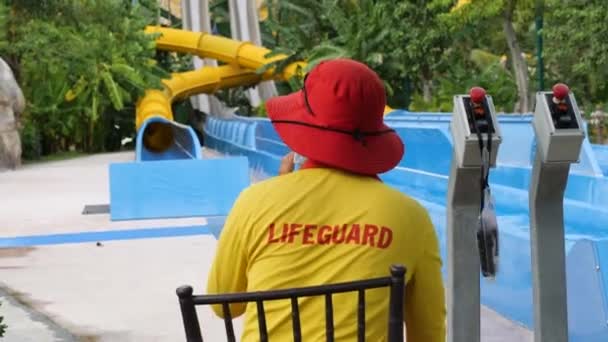 Vue arrière d'un maître nageur en uniforme dans un parc aquatique assis sur une chaise. — Video