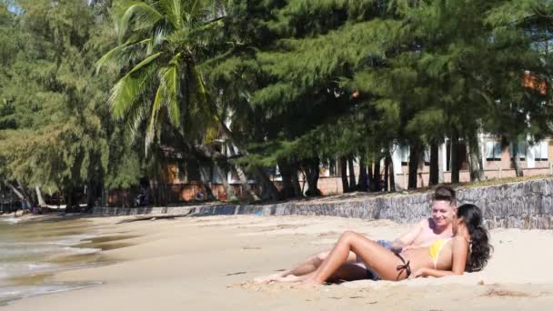 Alegre embarazada joven pareja acostada en la arena en la playa hablando y riendo. — Vídeo de stock