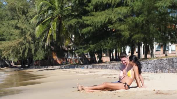Jovem casal grávida sentado na praia feliz falando e tocando barriga. — Vídeo de Stock