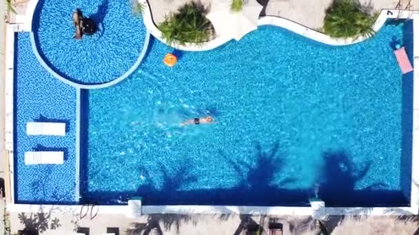 Vzdušný pohled shora dolů na muže plavajícího v modrém bazénu za slunečného dne. — Stock video
