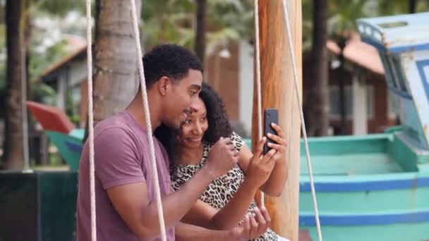 Ευτυχισμένο ζευγάρι κάθεται σε μια κούνια τραβώντας φωτογραφίες selfie μαζί από το smartphone. — Αρχείο Βίντεο