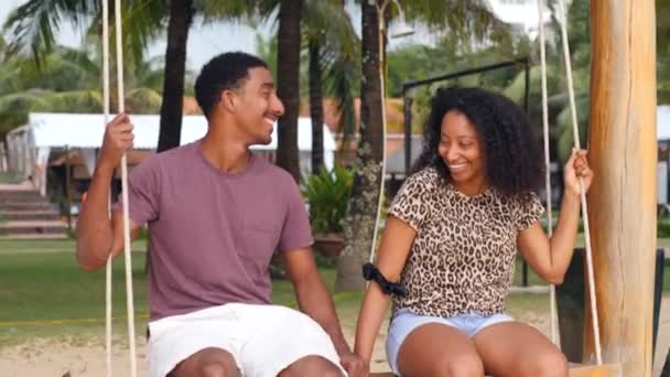 Casal romântico e feliz sentado em um balanço conversando e sorrindo um para o outro — Vídeo de Stock