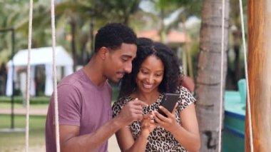 Salıncaktaki neşeli genç çift gülümsüyor, akıllı telefonuyla selfie çekiyorlar..