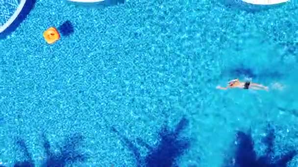 Uitzoomen vanuit de lucht uitzicht over een blauw zwembad met een man zwemmen in de voorkant kruipen stijl. — Stockvideo