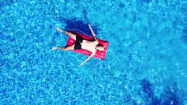 Drohnenbild eines kaukasischen Mannes auf einem aufblasbaren Bett, das im Schwimmbad schwimmt — Stockvideo
