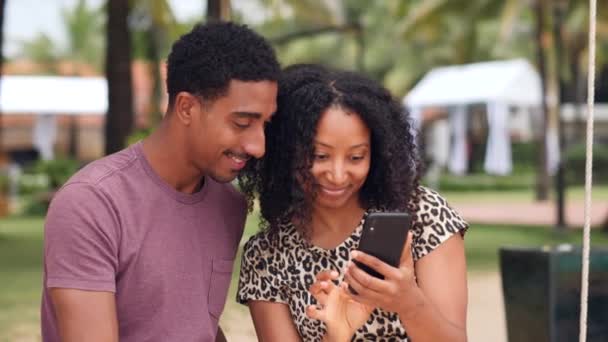 Ξέγνοιαστο αφρικανικό νεαρό ζευγάρι που παρακολουθεί ένα smartphone χαμογελώντας και γελώντας. — Αρχείο Βίντεο
