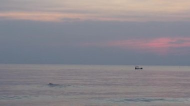 Alacakaranlıkta sahilin manzarasında yüzen bir adam ve suda hareket eden bir tekne..