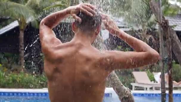 Widok z tyłu sexy mężczyzna biorąc prysznic na zewnątrz w pobliżu basenu w zwolnionym tempie strzał. — Wideo stockowe