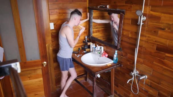 Młody biały mężczyzna myje zęby w umywalce w łazience przed lustrem — Wideo stockowe