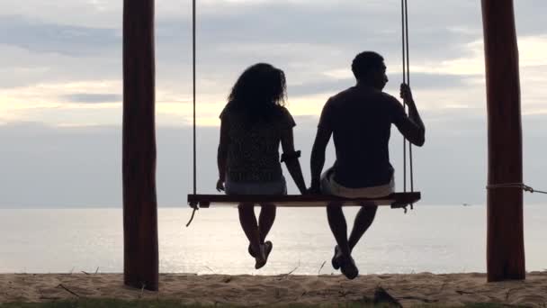 Rücken eines jungen Paares, das auf der Schaukel am Strand sitzt und plaudert und entspannt. — Stockvideo
