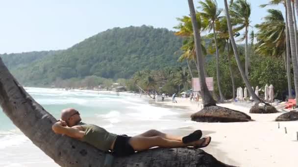 Kafkasyalı bir adam Asya 'da troipkal bir plajda Hindistan cevizi dalında dinleniyor ve yatıyor. — Stok video