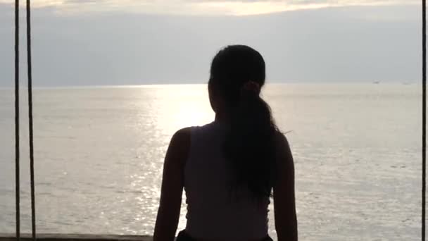 Közelről, egy fiatal nő háta mögött, aki hintázik és pihen a parton. — Stock videók