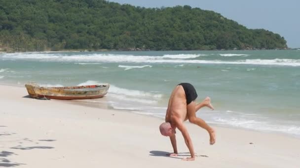 強いです白人男ありますhandstandヨガポーズで海岸で熱帯ビーチ — ストック動画