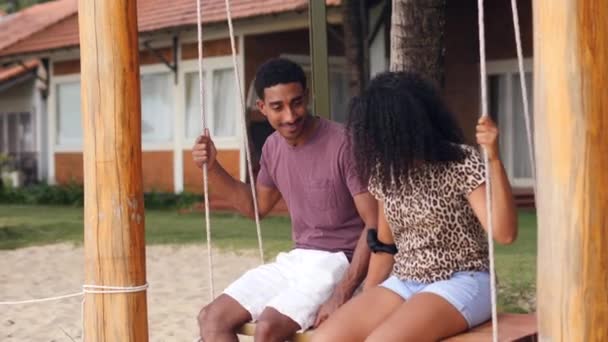 Romântico jovem casal africano balançando em um balanço de praia sorrindo e conversando. — Vídeo de Stock