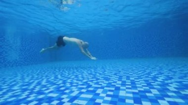 Mavi şeffaf yüzme havuzunda kısa yüzen beyaz adam.